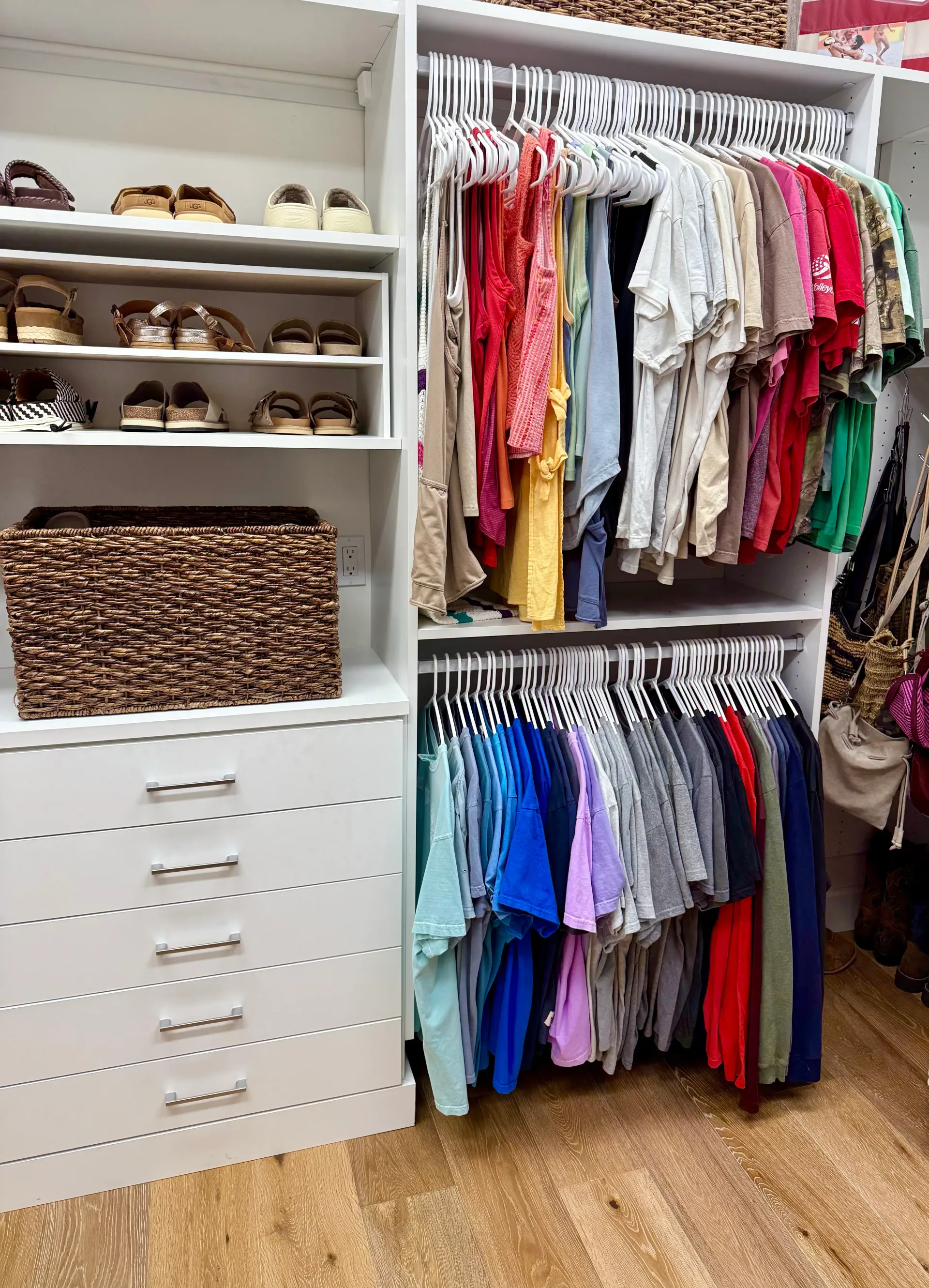 Organized white reach-in closet with color-coordinated clothing, shelving, footwear, and baskets